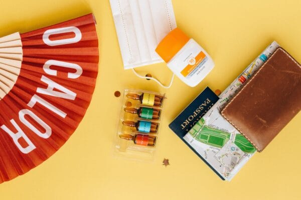 Flatlay of travel essentials like mask, vaccine, and sunscreen on yellow background