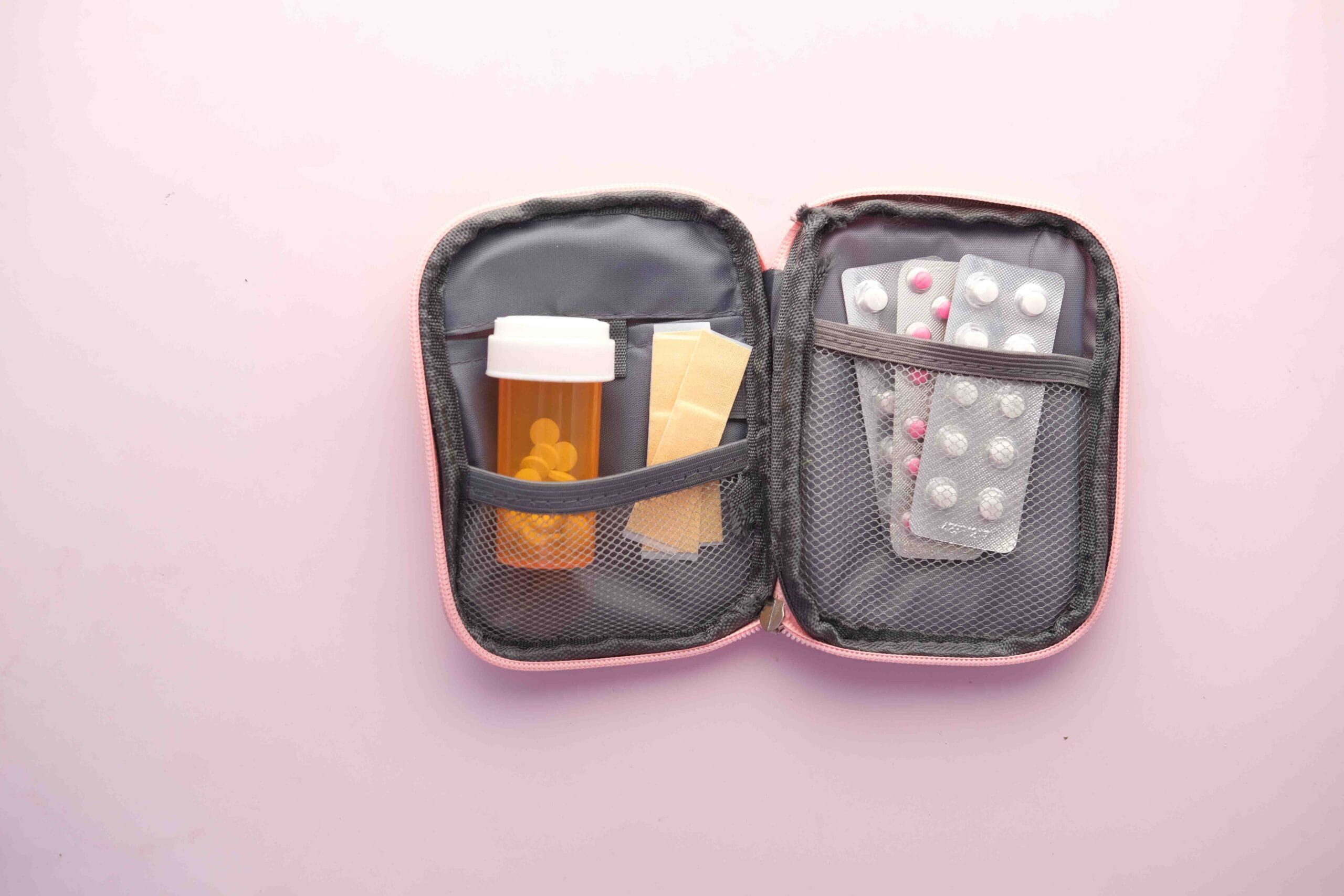 Carrying Medication Legally: A Practical Guide, Open first aid kit with pill bottle, blister packs, and band-aids on a pastel background.