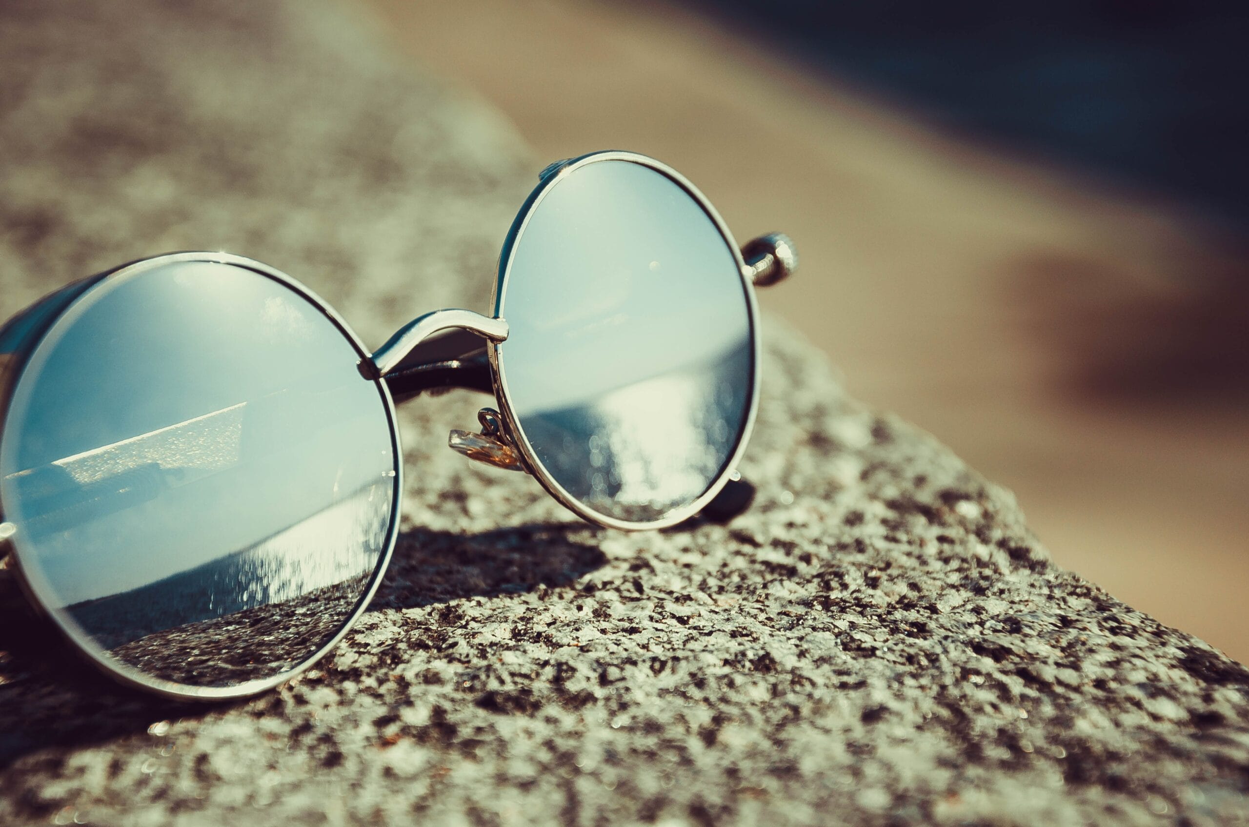Cruising With Low Vision or Blindness: A Complete Guide, Round sunglasses resting on a sandy beach reflecting the ocean view.