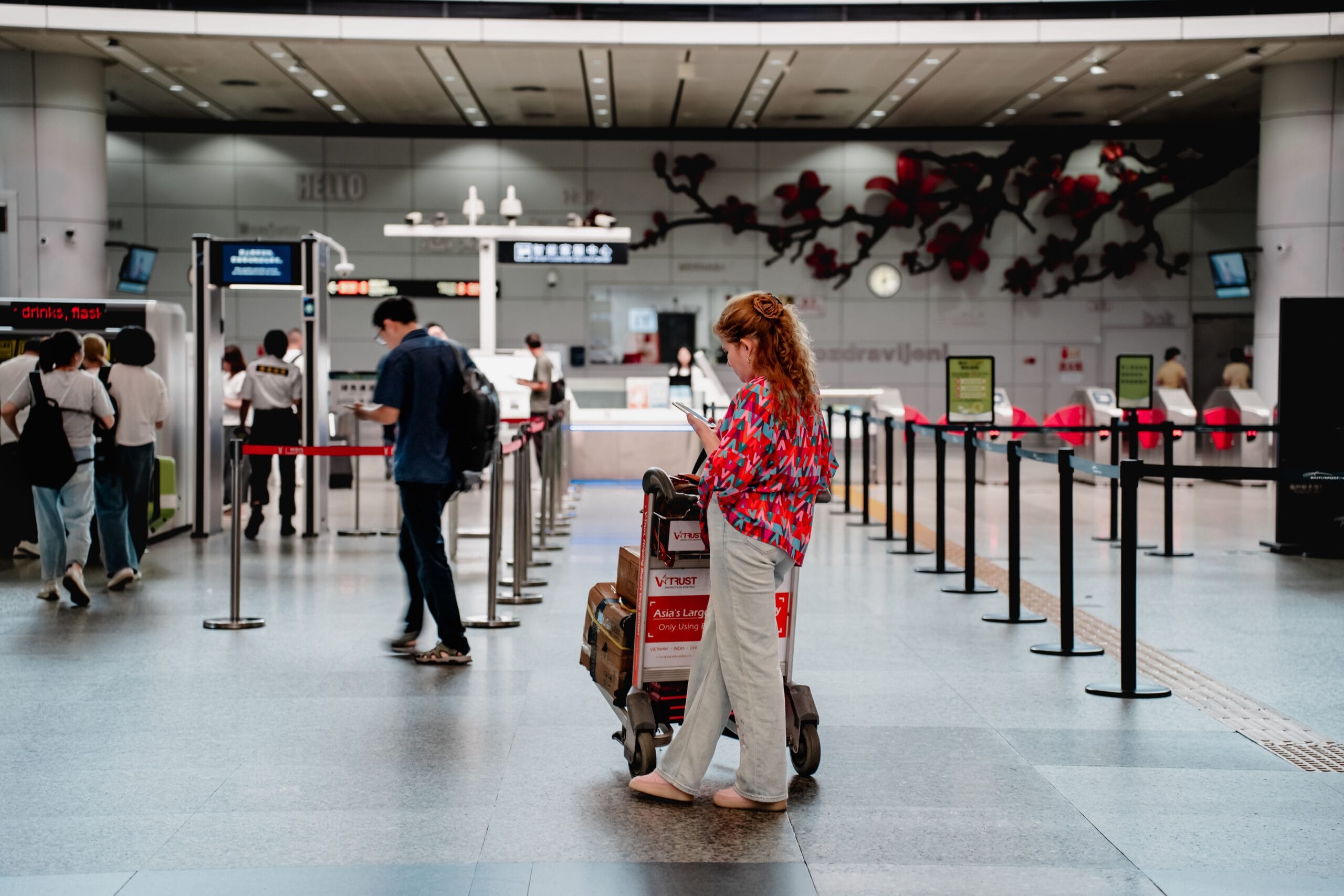 Navigating Airport Security With Medical Devices and Implants, A traveler checks her phone while waiting with a luggage cart at a busy airport terminal in Guangzhou.